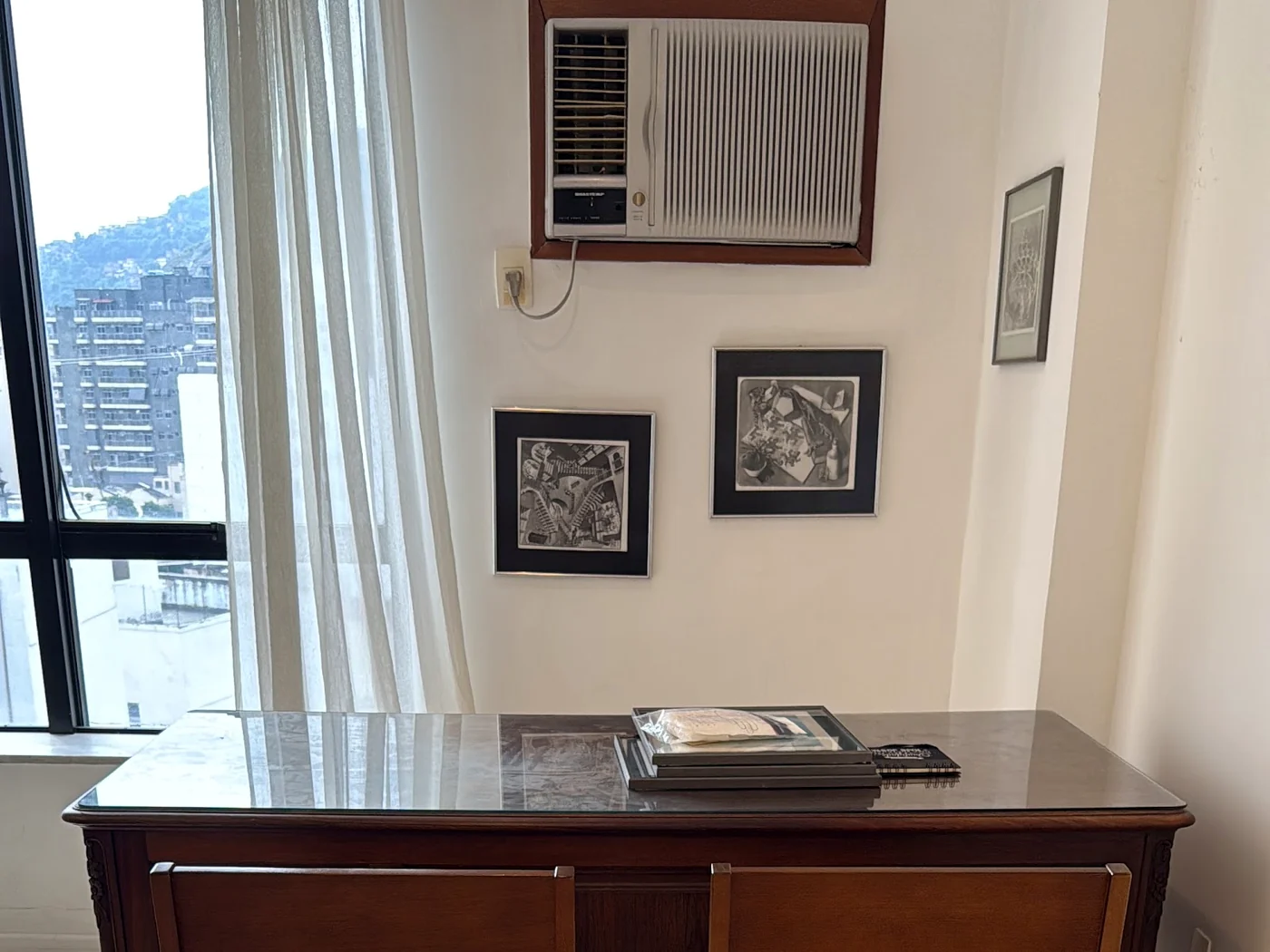 Canto da sala 1103: janela, dois quadros na parede, ar-condicionado e um console de madeira